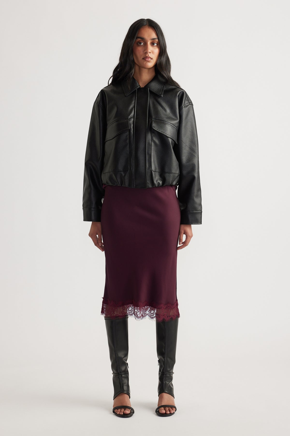 Woman wearing a burgundy lace-trim midi skirt with a black leather jacket and tall black boots