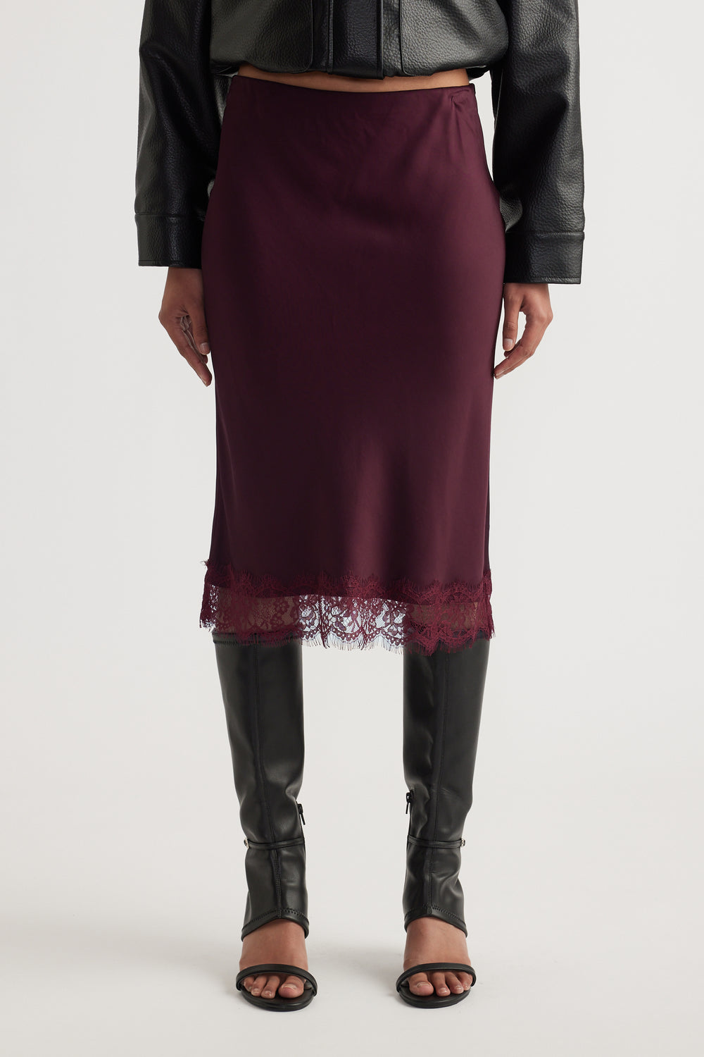 Woman wearing a burgundy satin midi skirt with lace trim, a black leather jacket and knee high boots