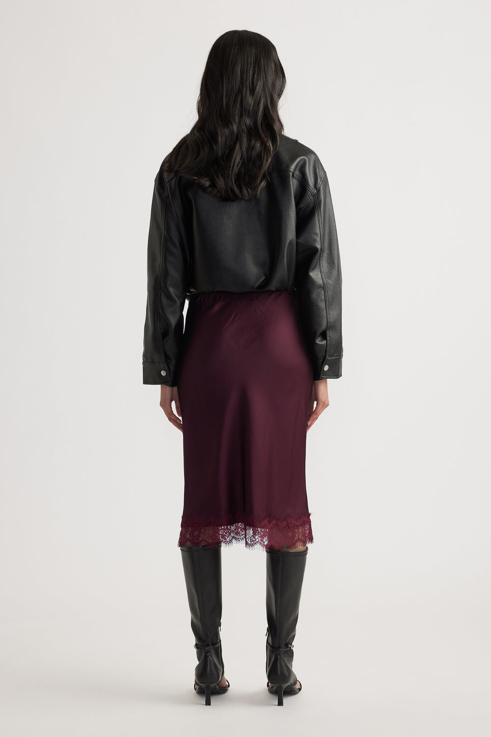 Back view of woman wearing a burgundy lace trim midi skirt with a black leather jacket and knee high boots