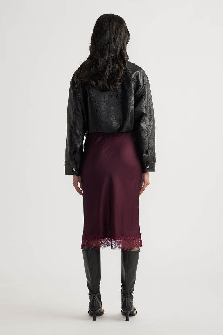 Back view of woman wearing a burgundy lace trim midi skirt with a black leather jacket and knee high boots