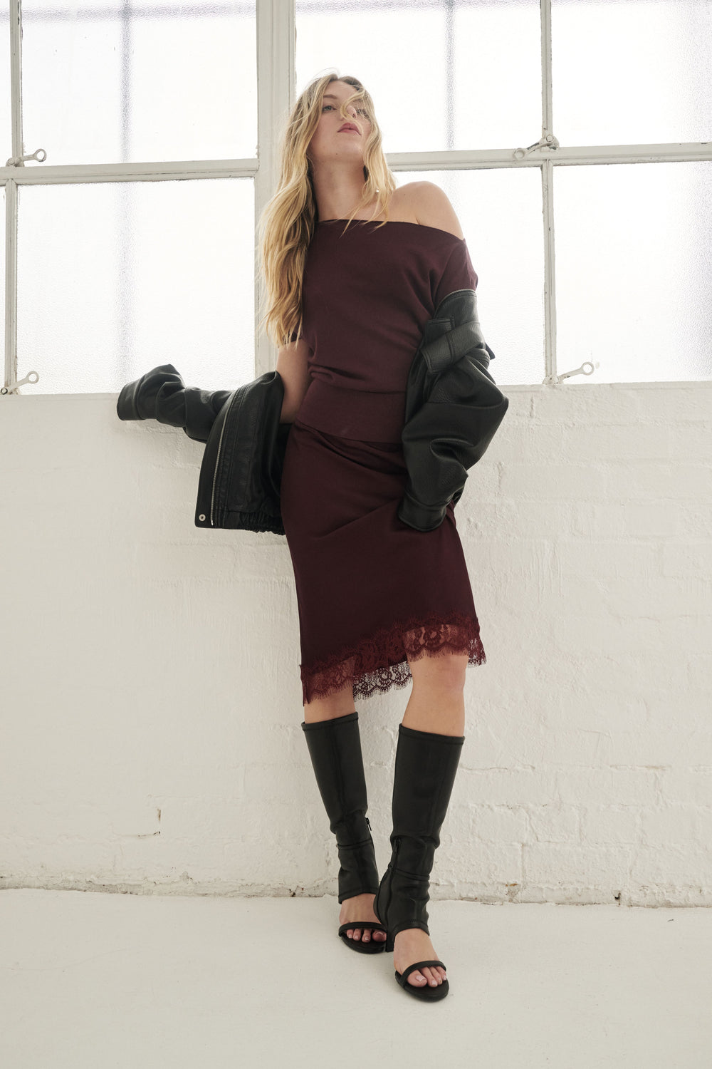 Woman wearing a burgundy lace-trim midi skirt with an off shoulder top, black jacket and knee-high boots