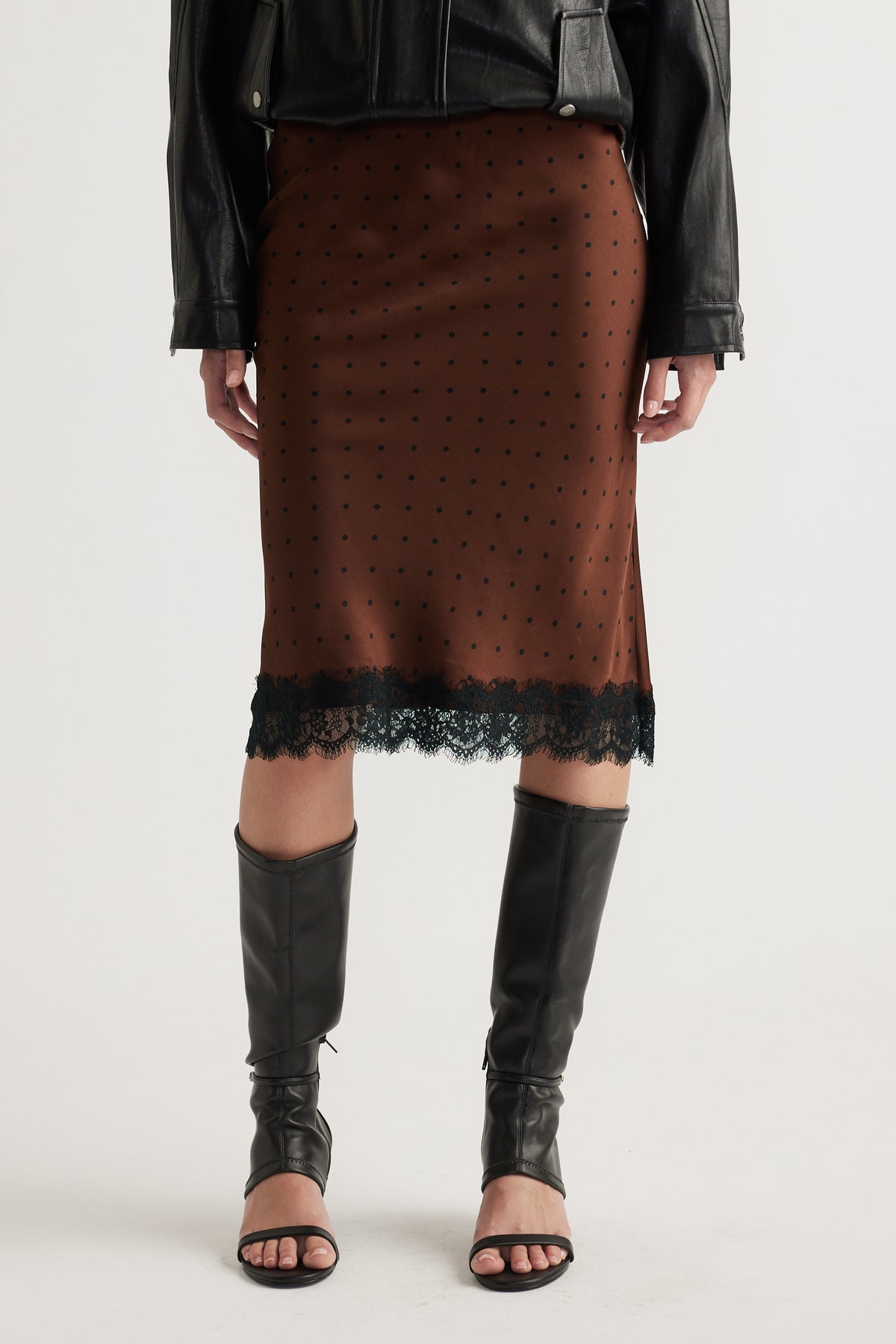 Front view of woman wearing brown midi skirt with black lace trim paired with leather jacket and knee-high boots