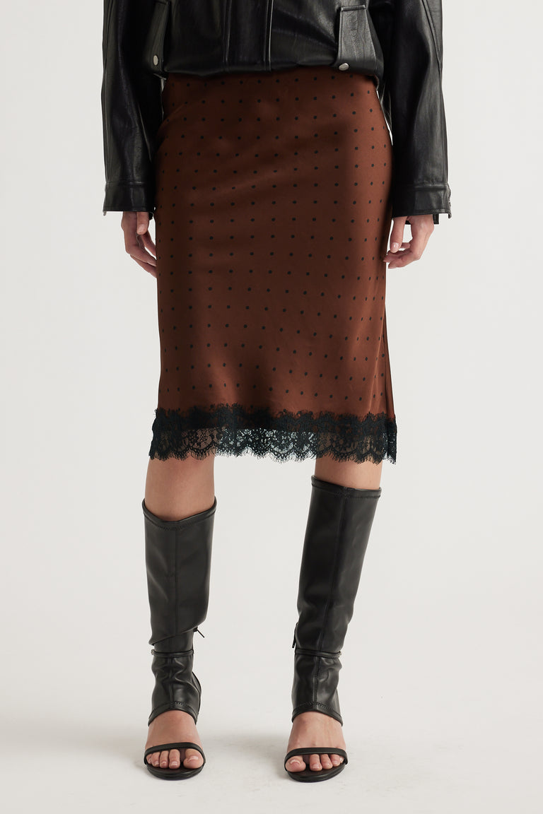 Front view of woman wearing brown midi skirt with black lace trim paired with leather jacket and knee-high boots