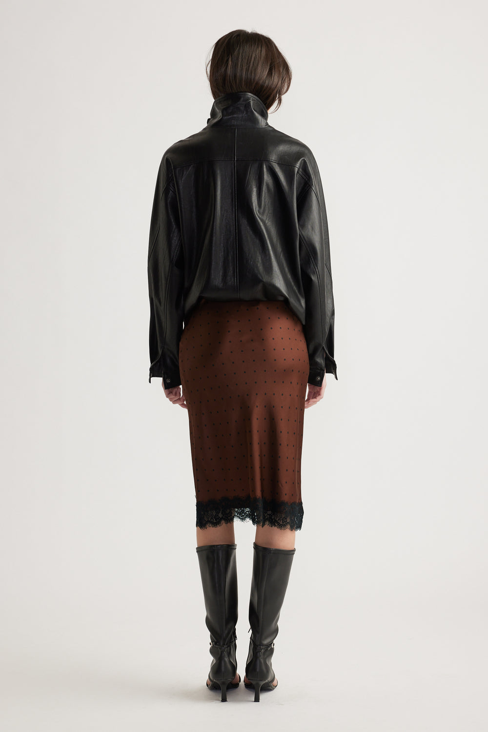 Rear view of woman wearing brown midi skirt with lace trim, paired with black leather jacket and knee-high boots