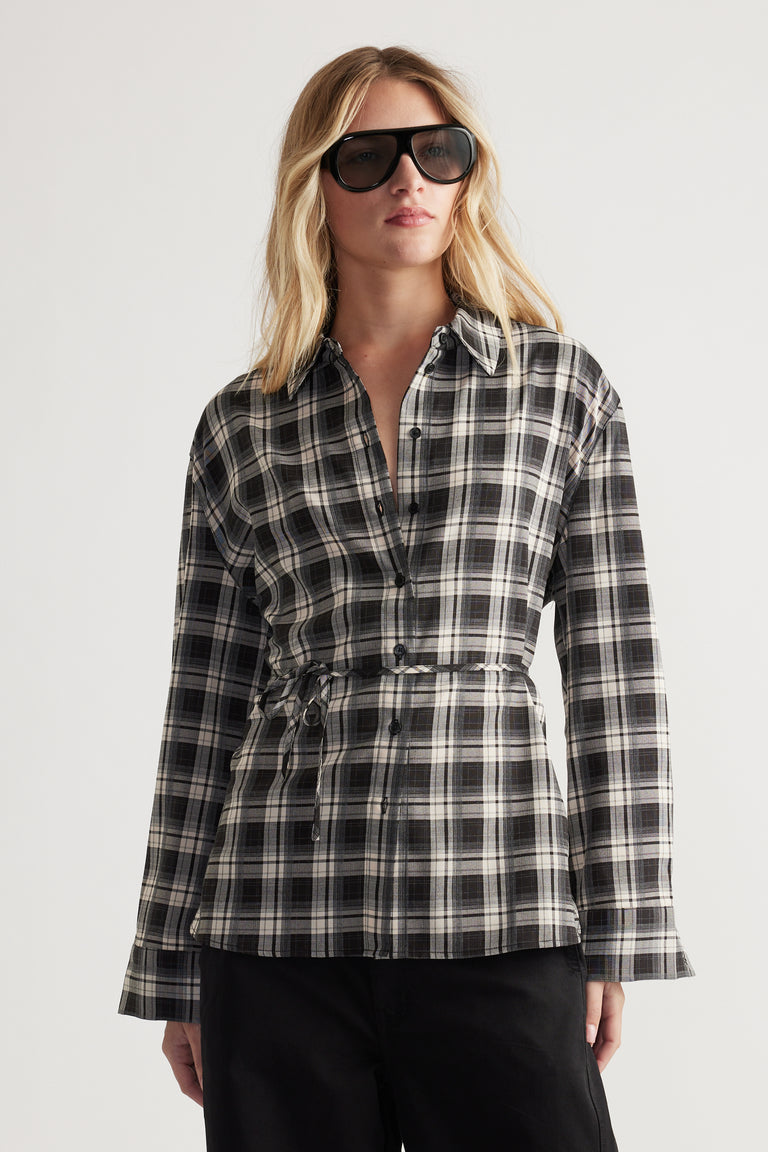 Woman wearing a black and white checked shirt with a tie waist detail, styled with black pants and oversized sunglasses