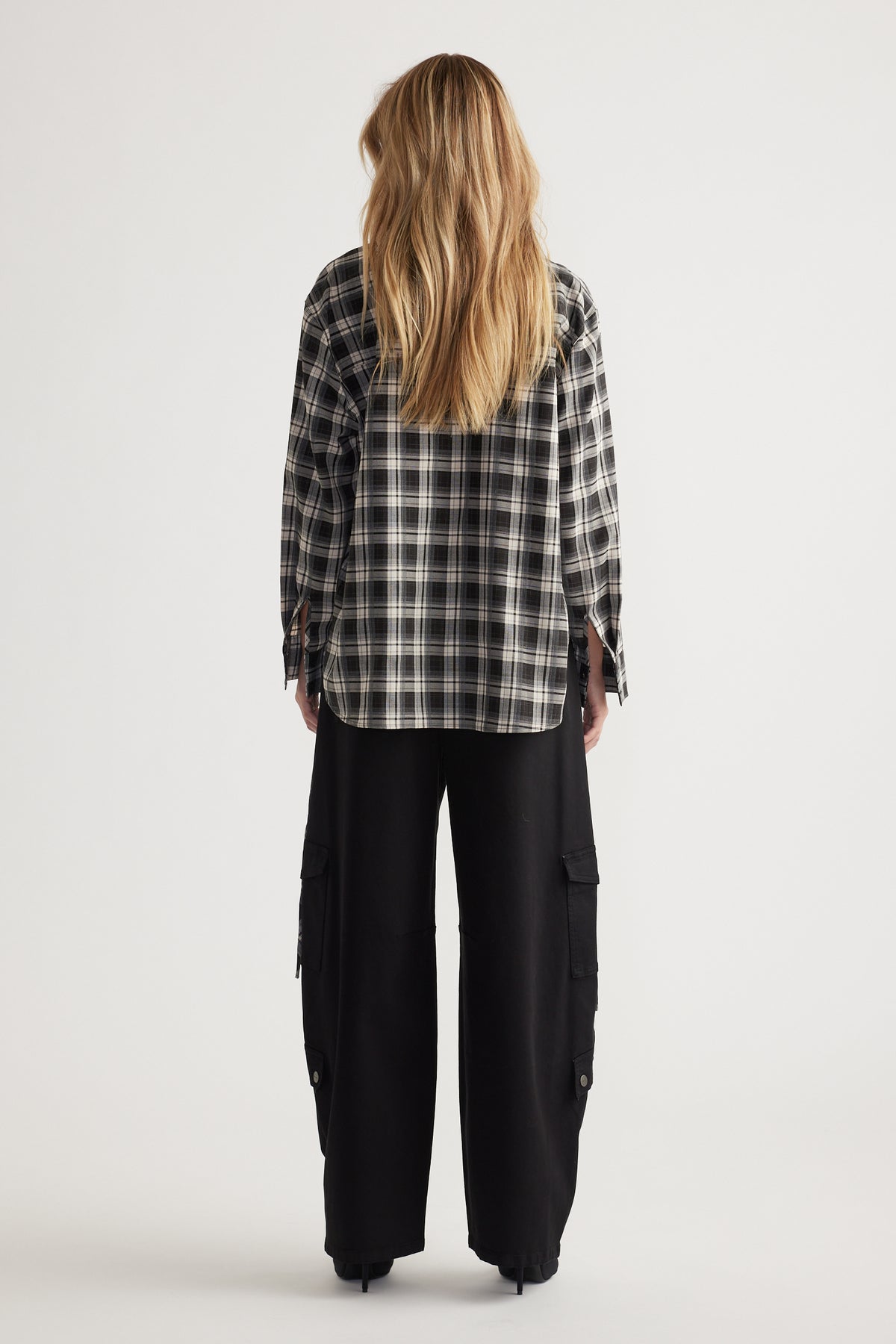 Back view of a woman wearing a relaxed black and white checked shirt paired with loose black cargo pants