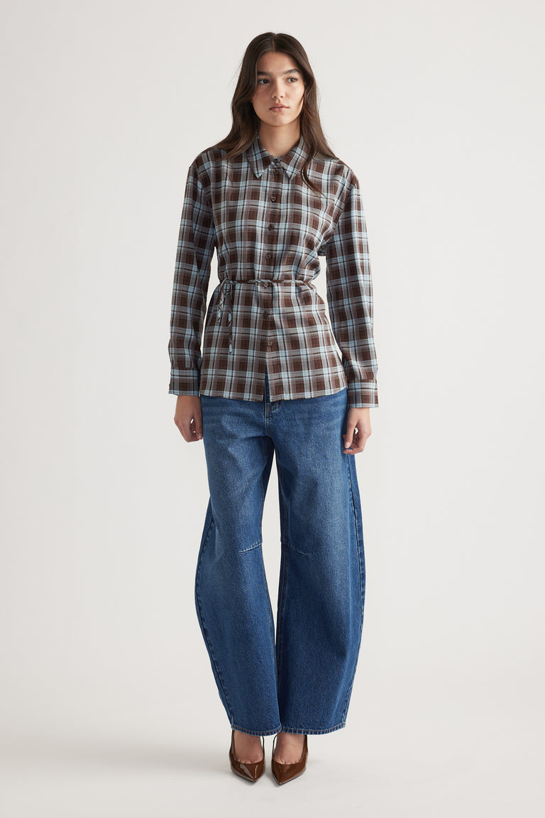 Woman wearing a tailored checked shirt in brown and blue tones paired with wide-leg denim jeans and brown pointed heels