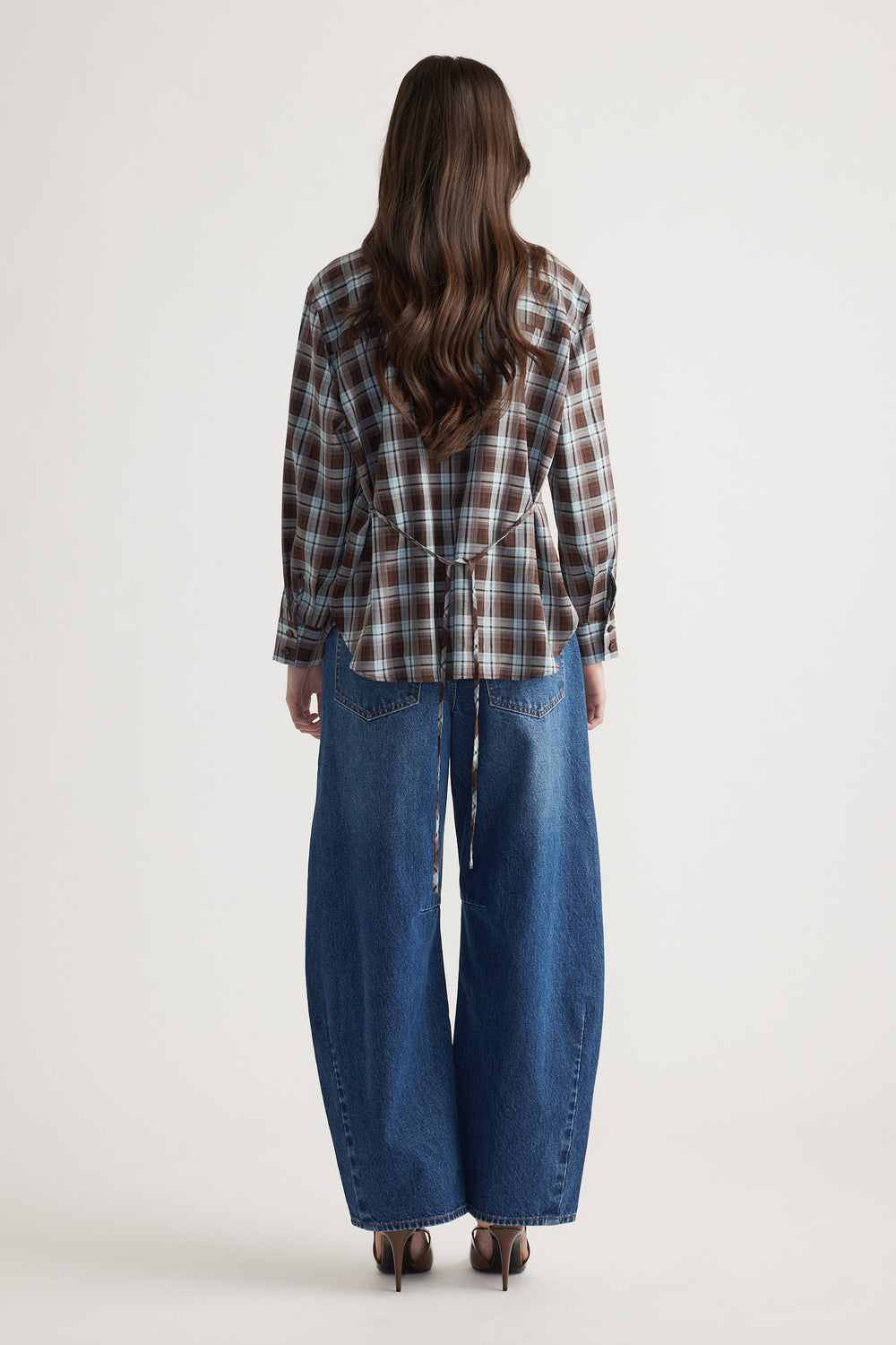 Woman wearing a brown and blue check shirt with a back tie detail paired with wide-leg blue denim jeans and heels, rear view