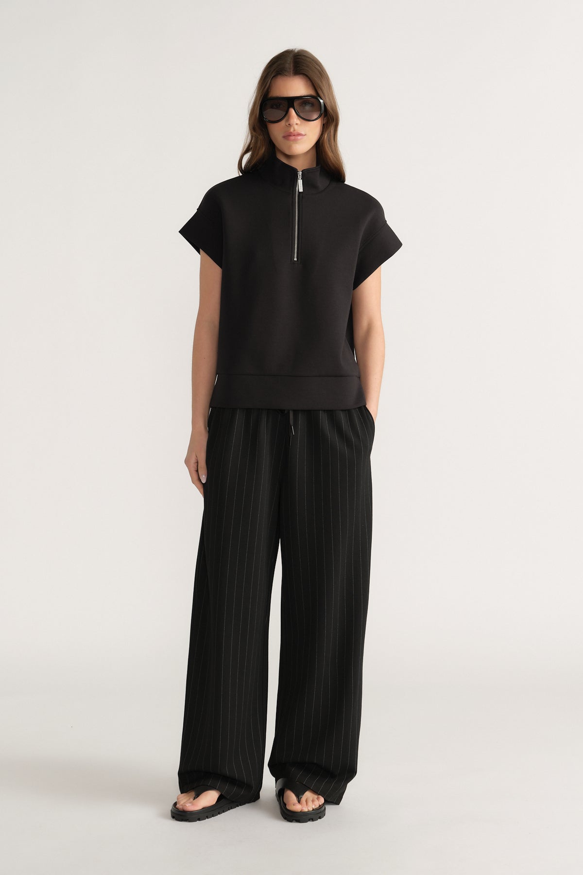 Woman wearing a black half zip top with wide leg pleated pants and sunglasses