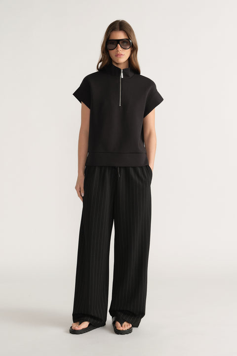 Woman wearing a black half zip top with wide leg pleated pants and sunglasses