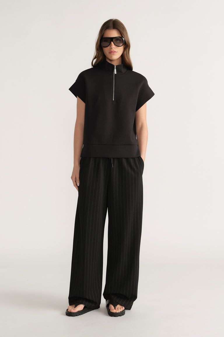 Woman wearing a black half zip top with wide leg pleated pants and sunglasses
