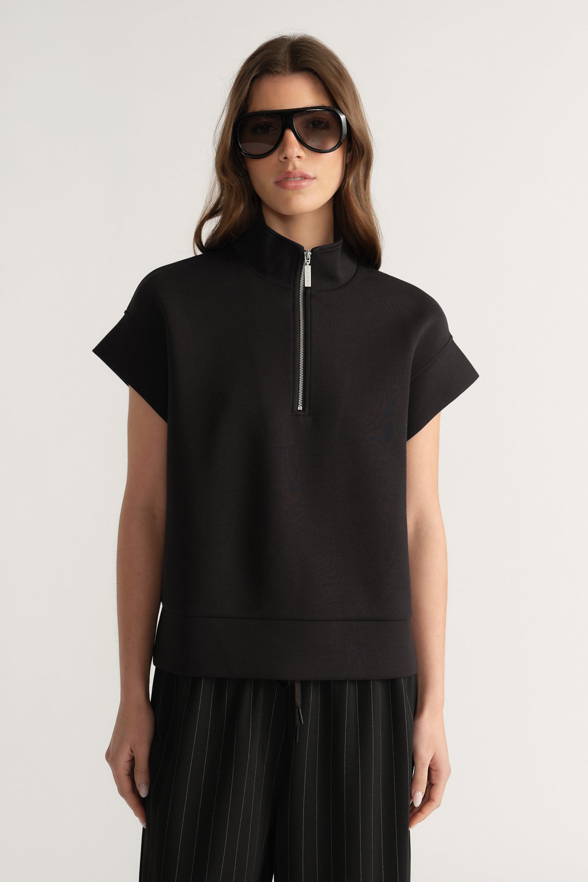 Woman wearing a black short sleeve half zip funnel neck top with pleated black pants
