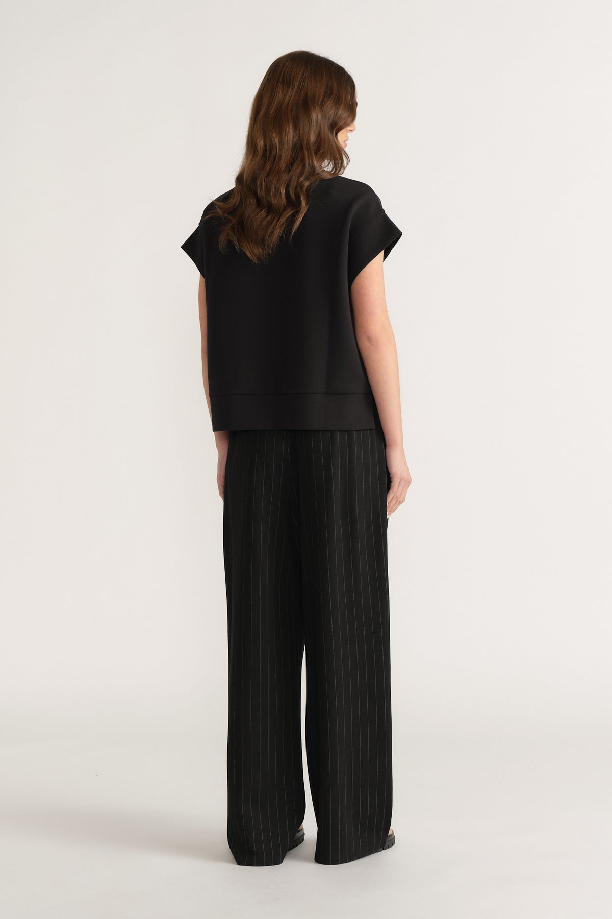 Back view of a woman wearing a black short sleeve top with black wide leg pleated pants