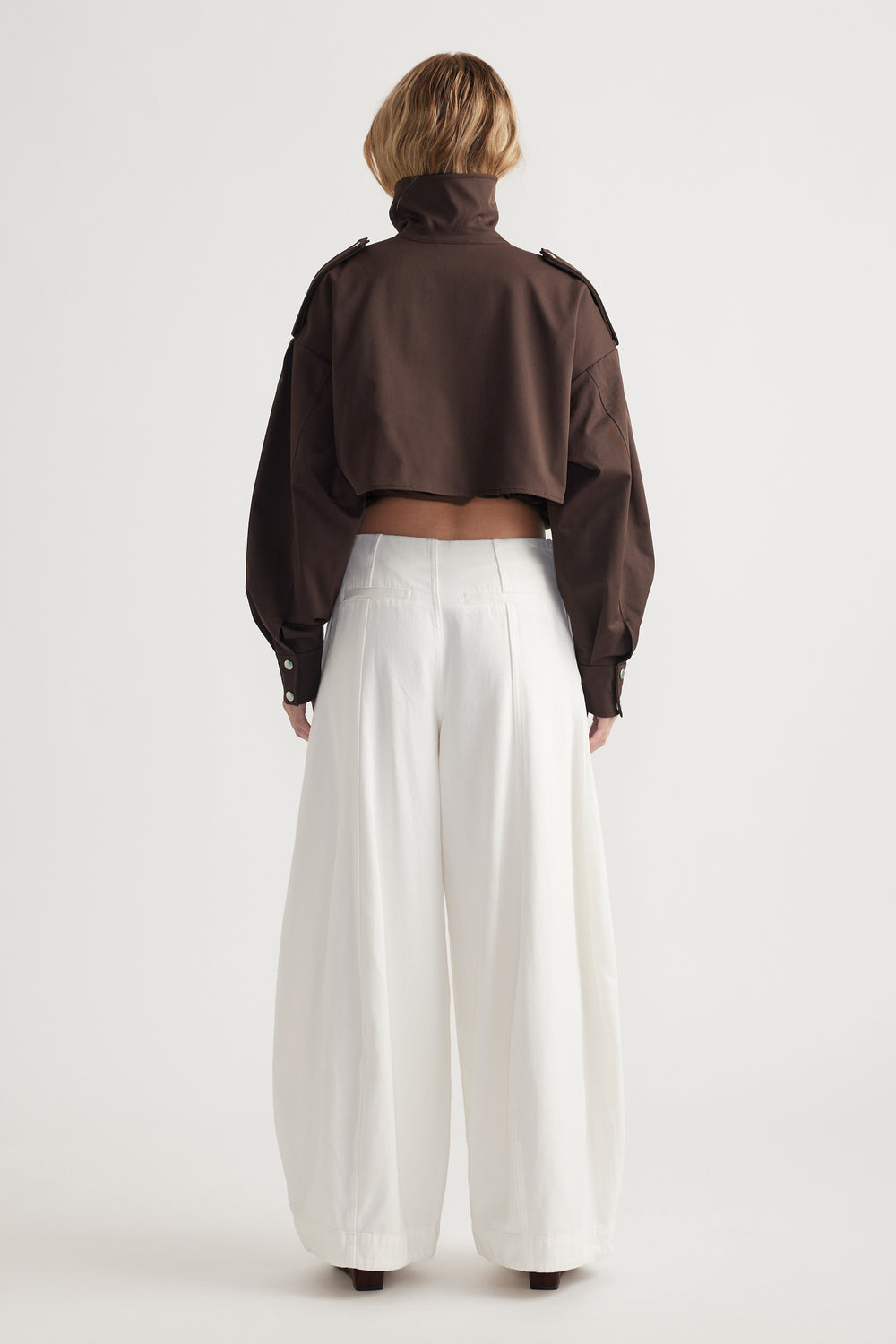 Woman seen from back wearing wide-leg white trousers paired with a cropped brown jacket with a high collar