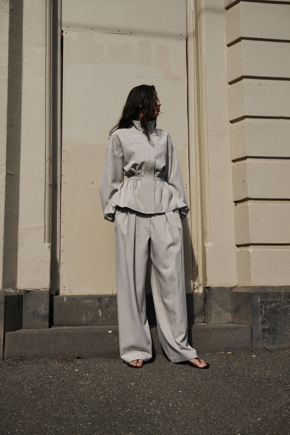 Woman wearing grey pleated wide leg pants with a matching tailored top and open toe shoes