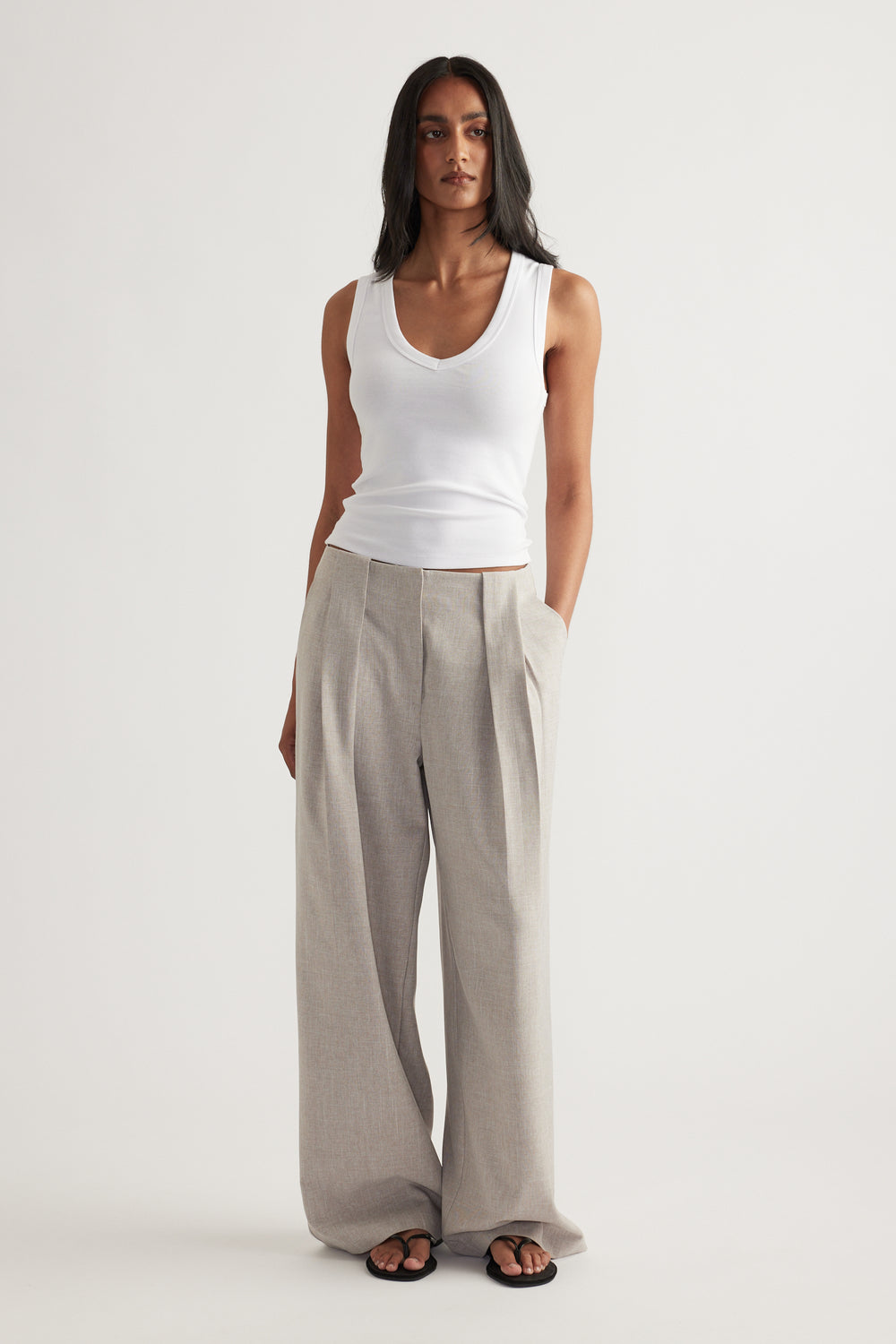 Woman wearing grey pleated wide-leg pants with a white tank top and black sandals