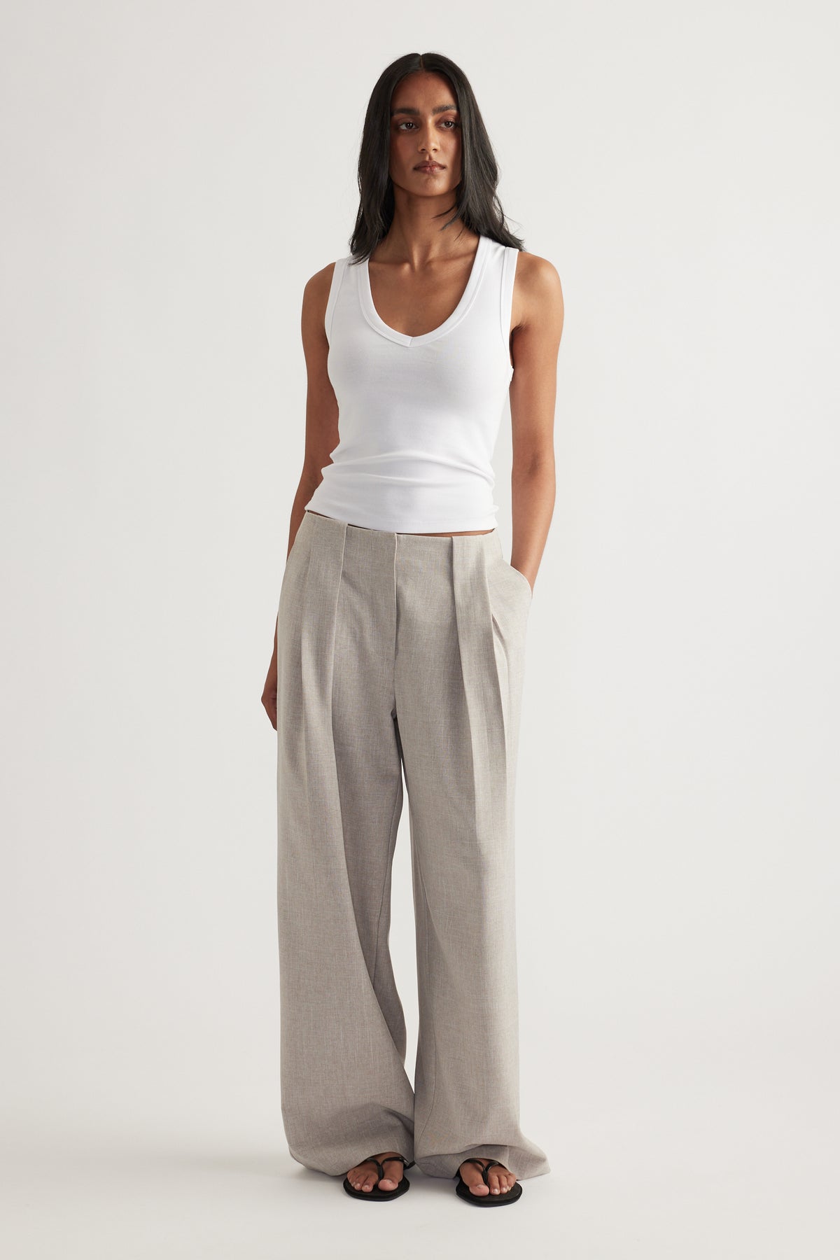 Woman wearing grey pleated wide-leg pants with a white tank top and black sandals