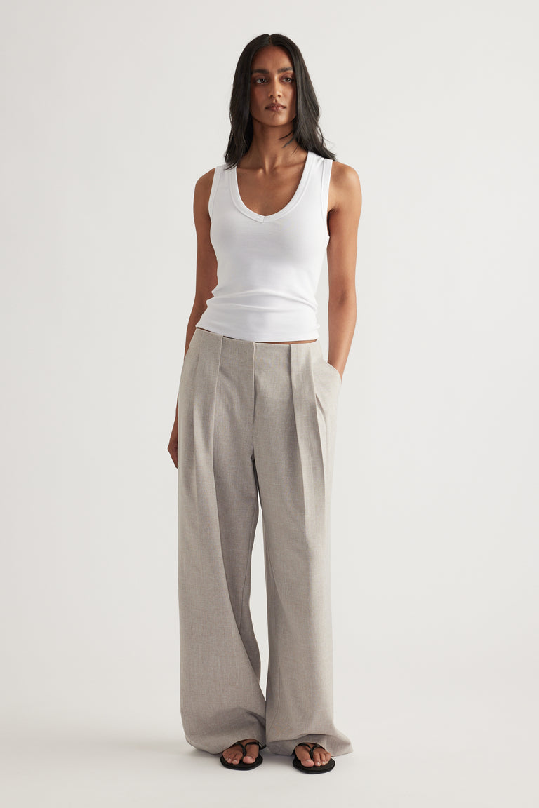Woman wearing grey pleated wide-leg pants with a white tank top and black sandals