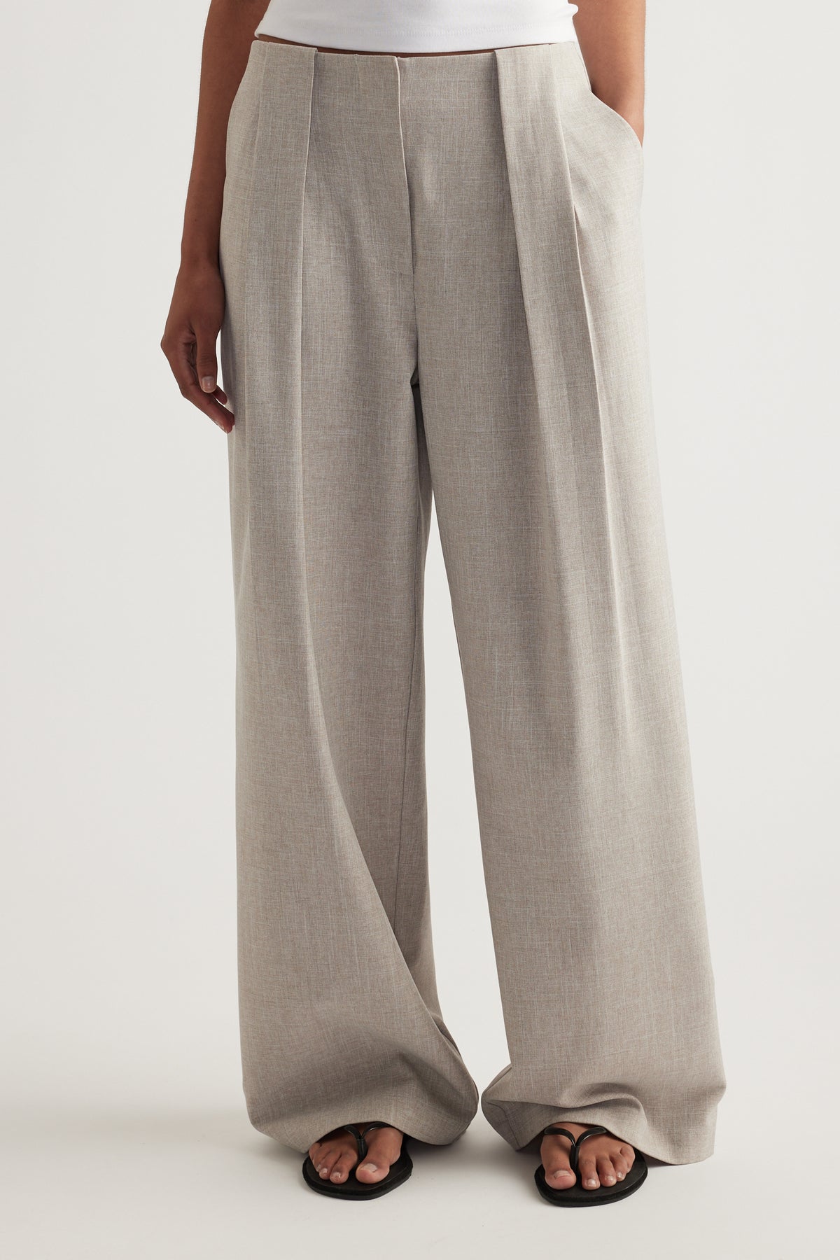Woman wearing taupe pleated wide-leg pants with side pockets and black sandals