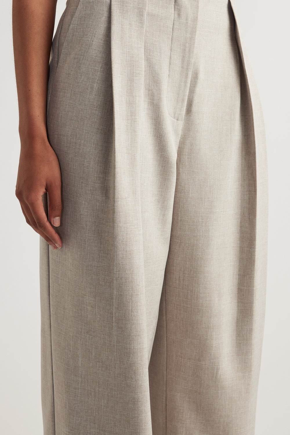 Close-up of a woman wearing cream wide-leg pants with pleat detailing