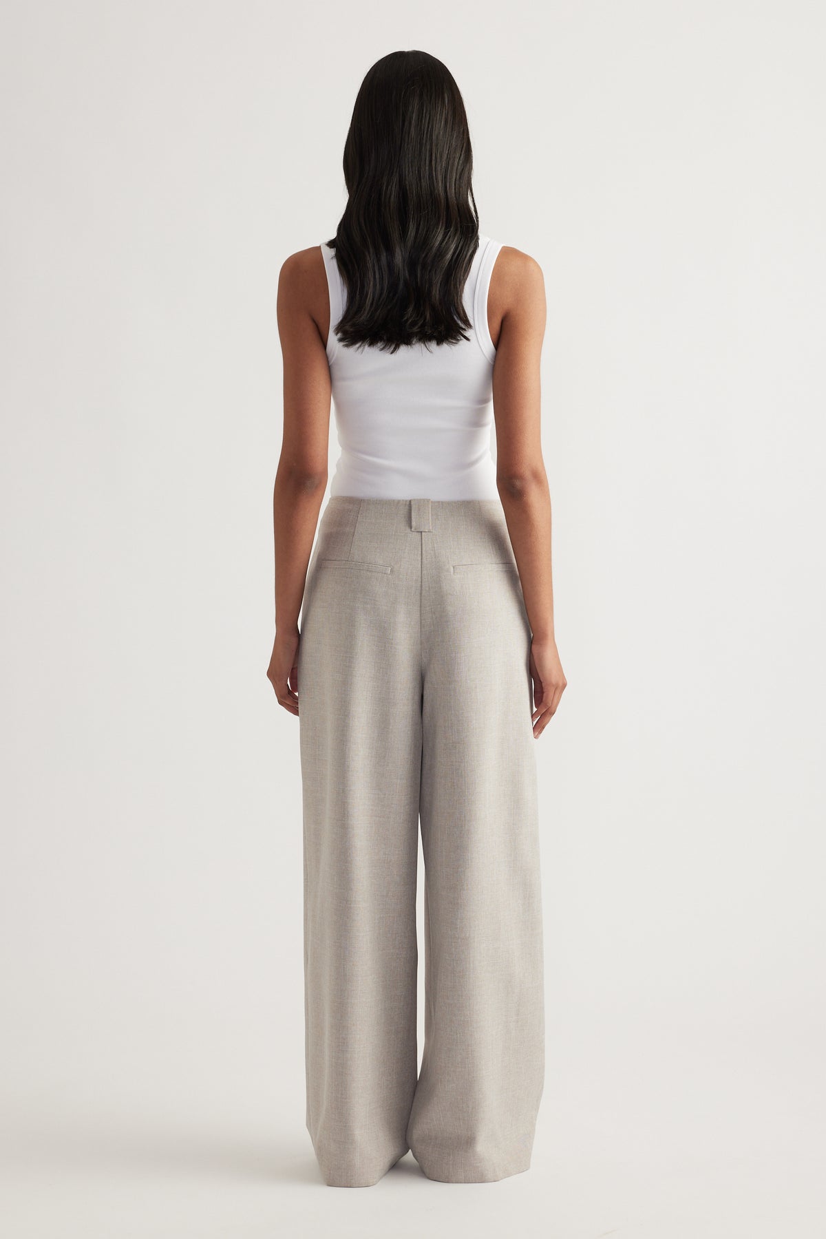 Back view of a woman wearing beige pleated wide leg pants with a fitted white tank top