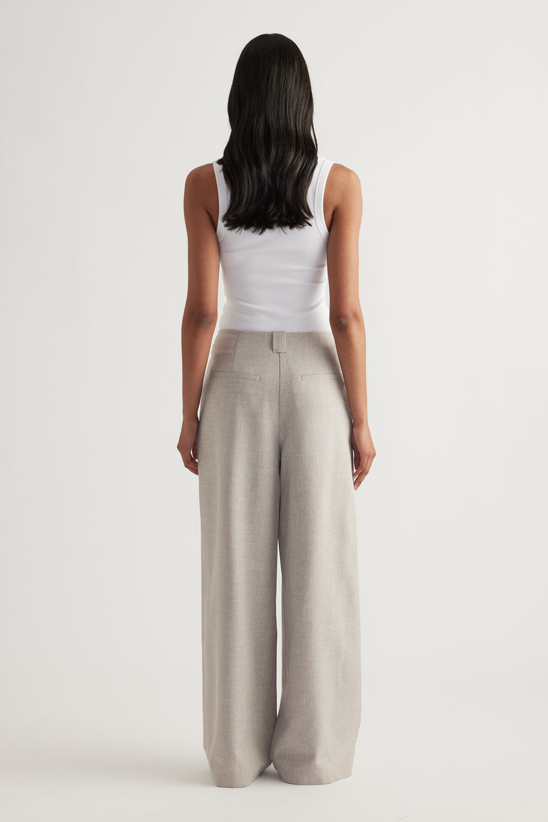 Back view of a woman wearing beige pleated wide leg pants with a fitted white tank top