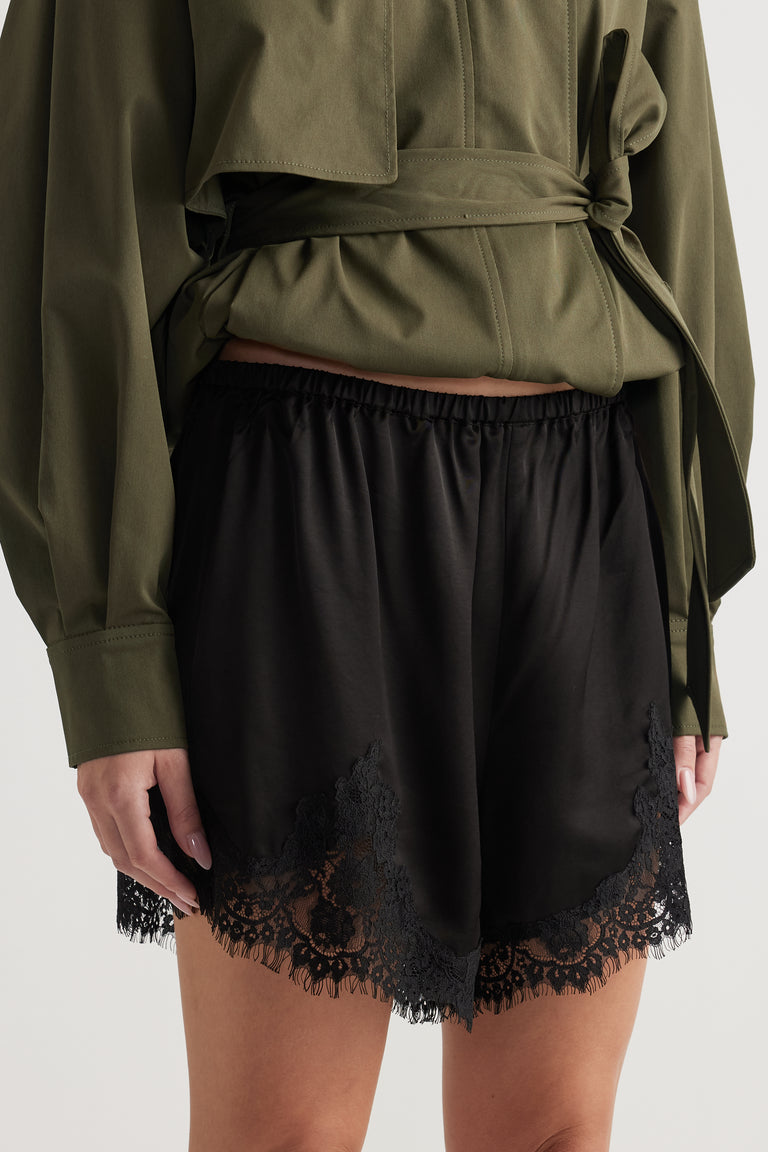 Woman wearing black satin shorts with delicate lace trim paired with an olive green tied blouse for a chic look