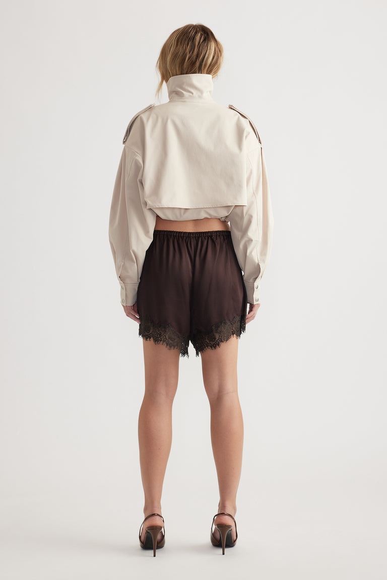 Back view of woman wearing black lace-trimmed satin shorts paired with cropped beige jacket and heels