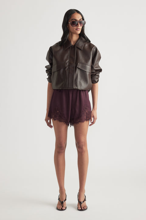 Woman wearing dark satin shorts with lace trim and a brown leather jacket