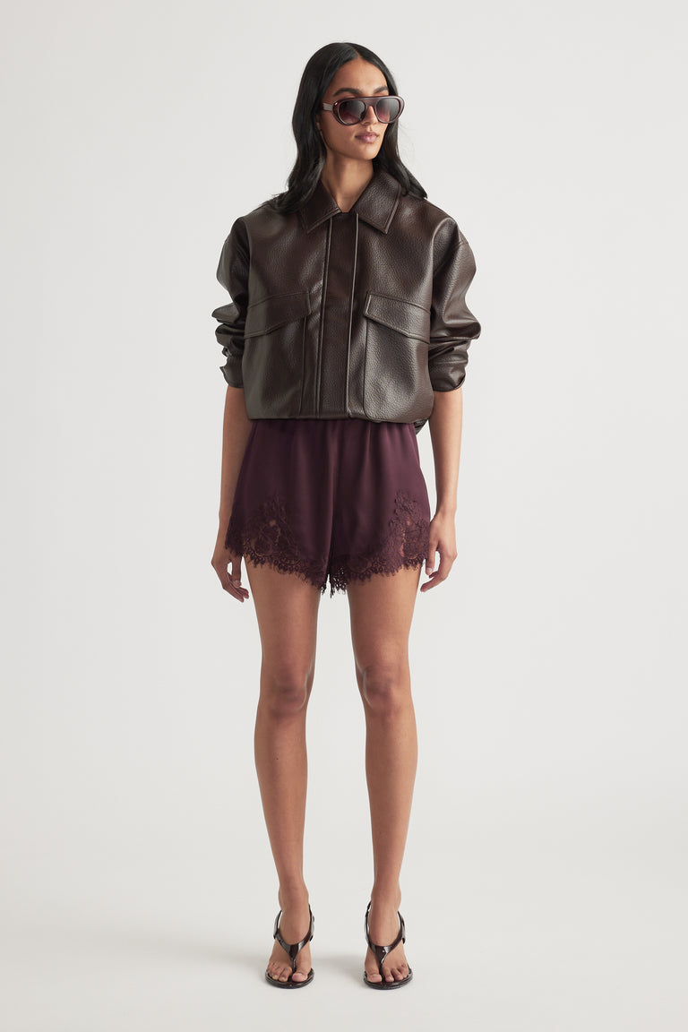 Woman wearing dark satin shorts with lace trim and a brown leather jacket