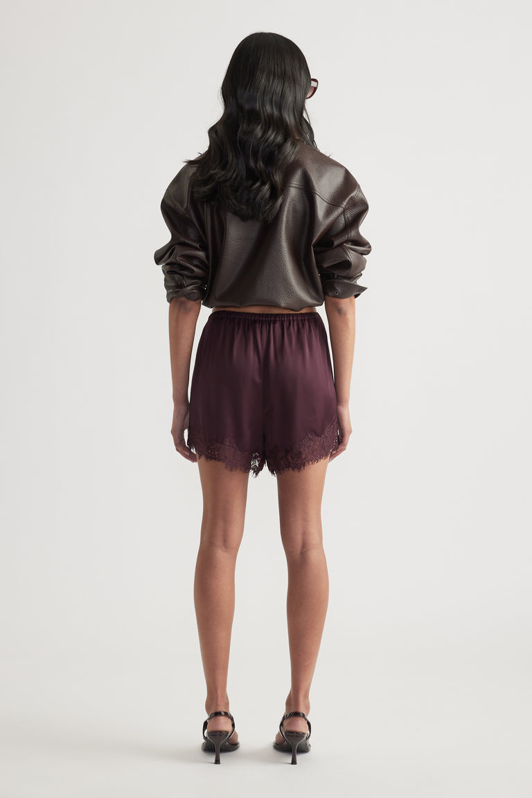 Woman wearing burgundy satin shorts with lace trim and an oversized leather jacket