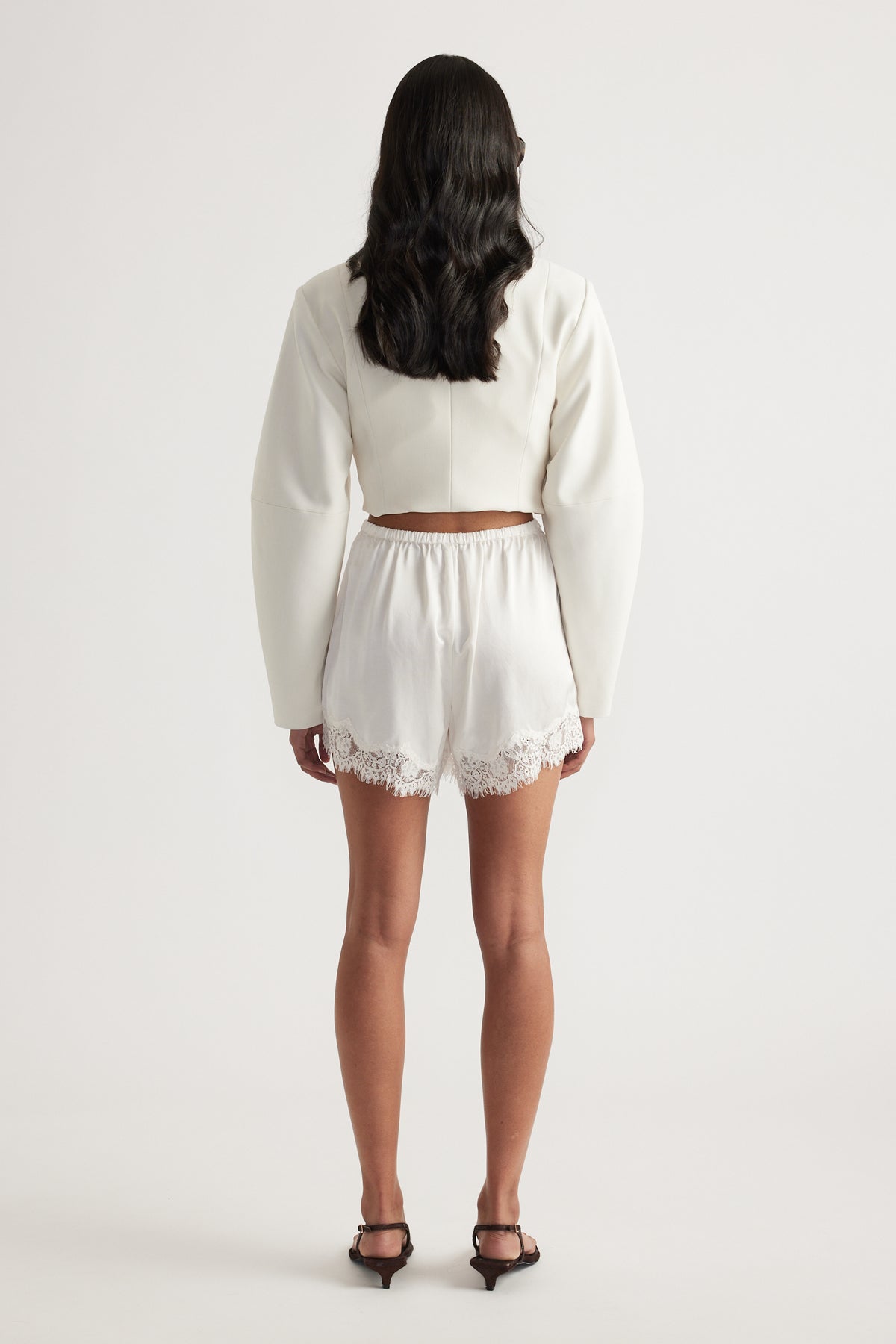 Woman wearing ivory satin shorts with an elastic waist and lace trim cropped above the knee