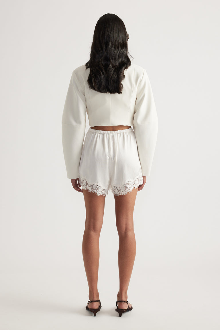 Woman wearing ivory satin shorts with an elastic waist and lace trim cropped above the knee