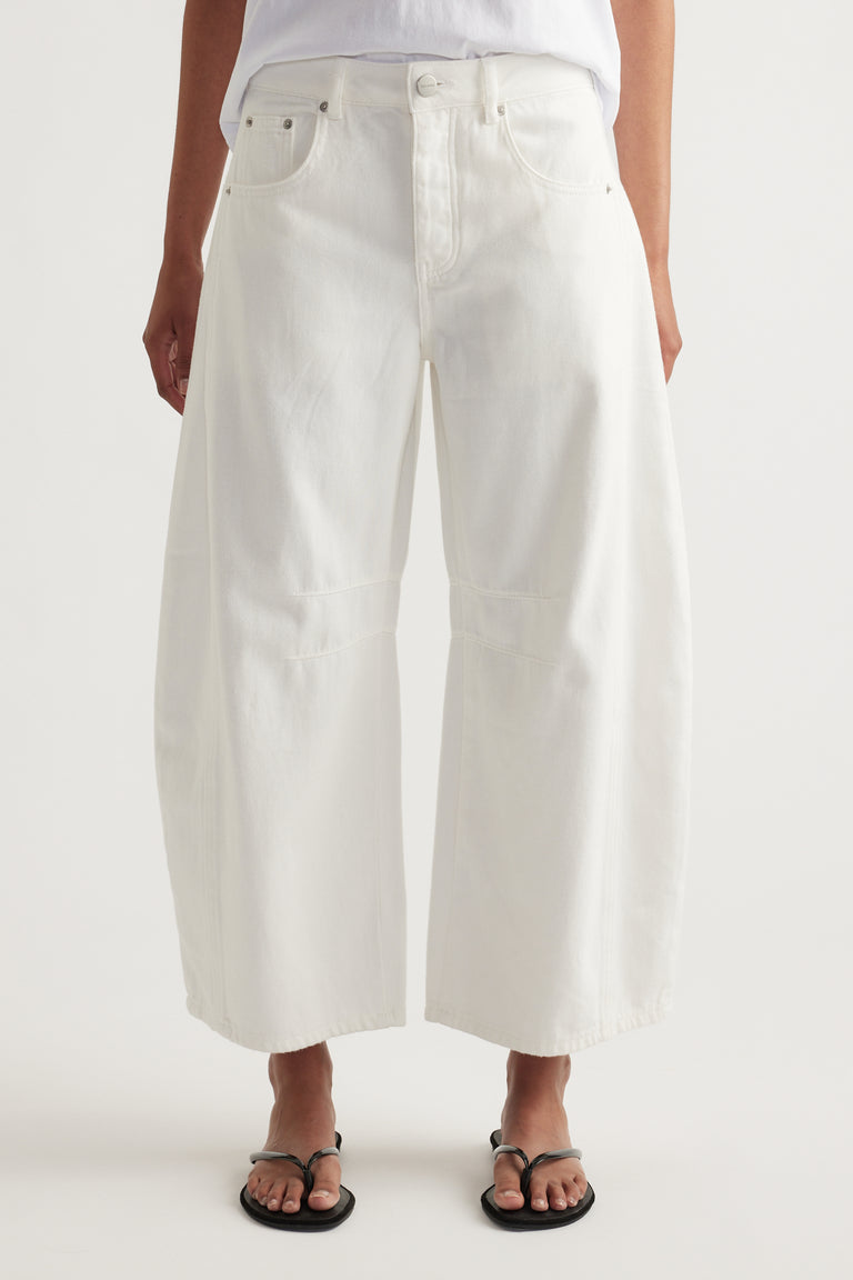 Model wearing white high rise barrel-leg jeans with a cropped length and relaxed curved silhouette