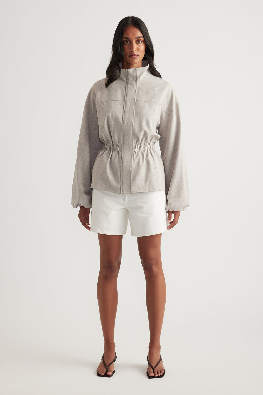 Woman wearing white denim shorts with a beige zip-front jacket and sandals