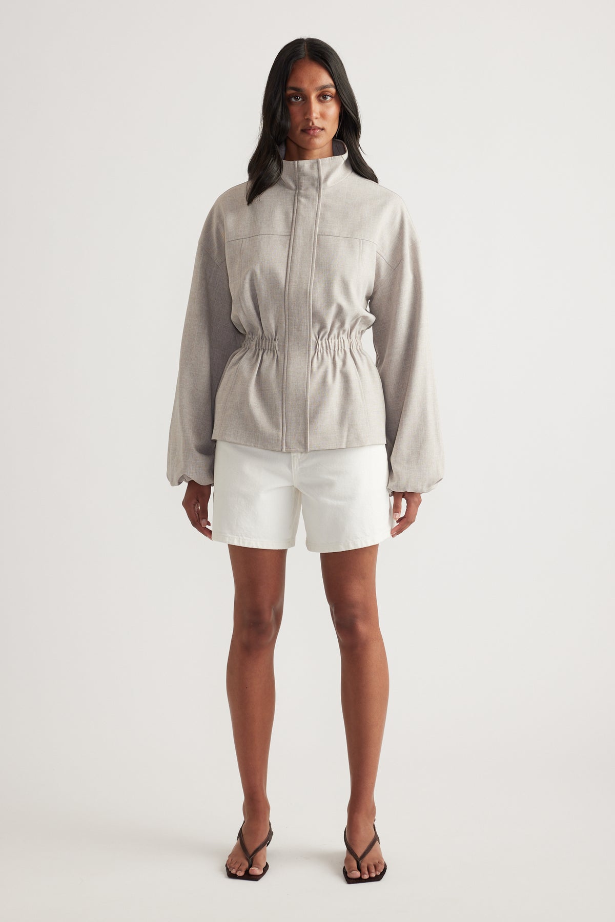 Woman wearing white denim shorts with a beige zip-front jacket and sandals