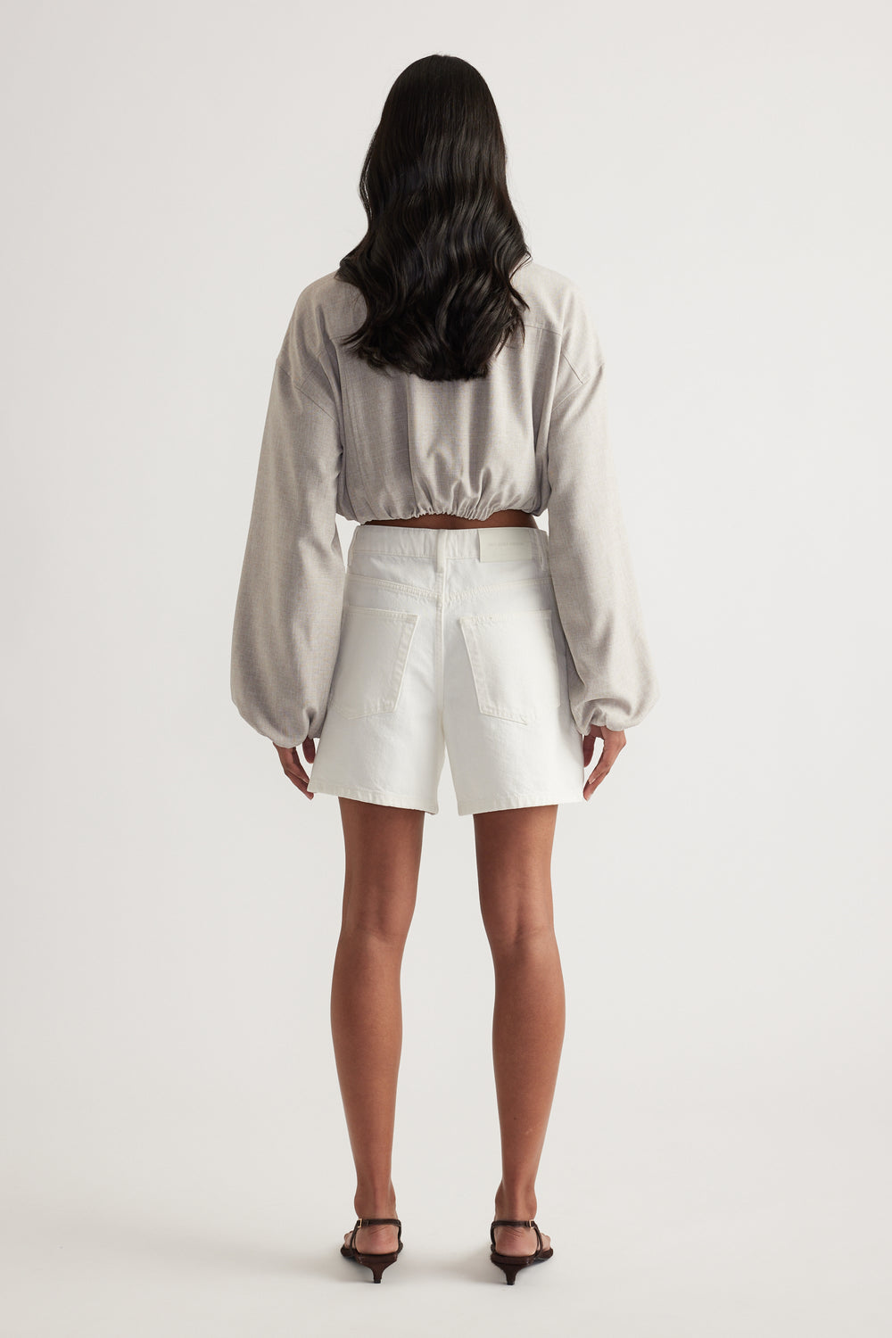 Woman wearing white high-rise A-line denim shorts with a cropped long-sleeve top, viewed from behind