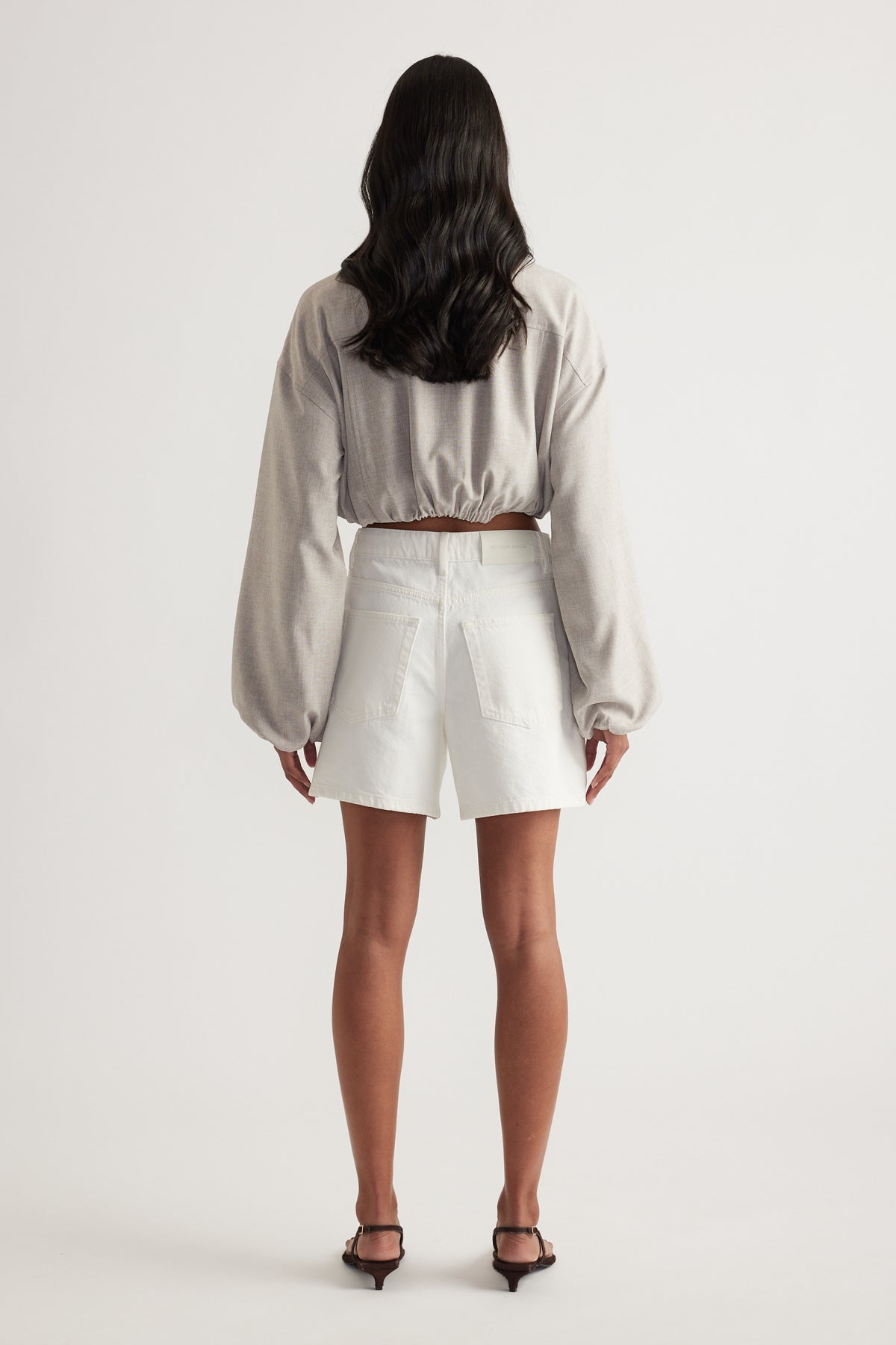 Woman wearing white high-rise A-line denim shorts with a cropped long-sleeve top, viewed from behind