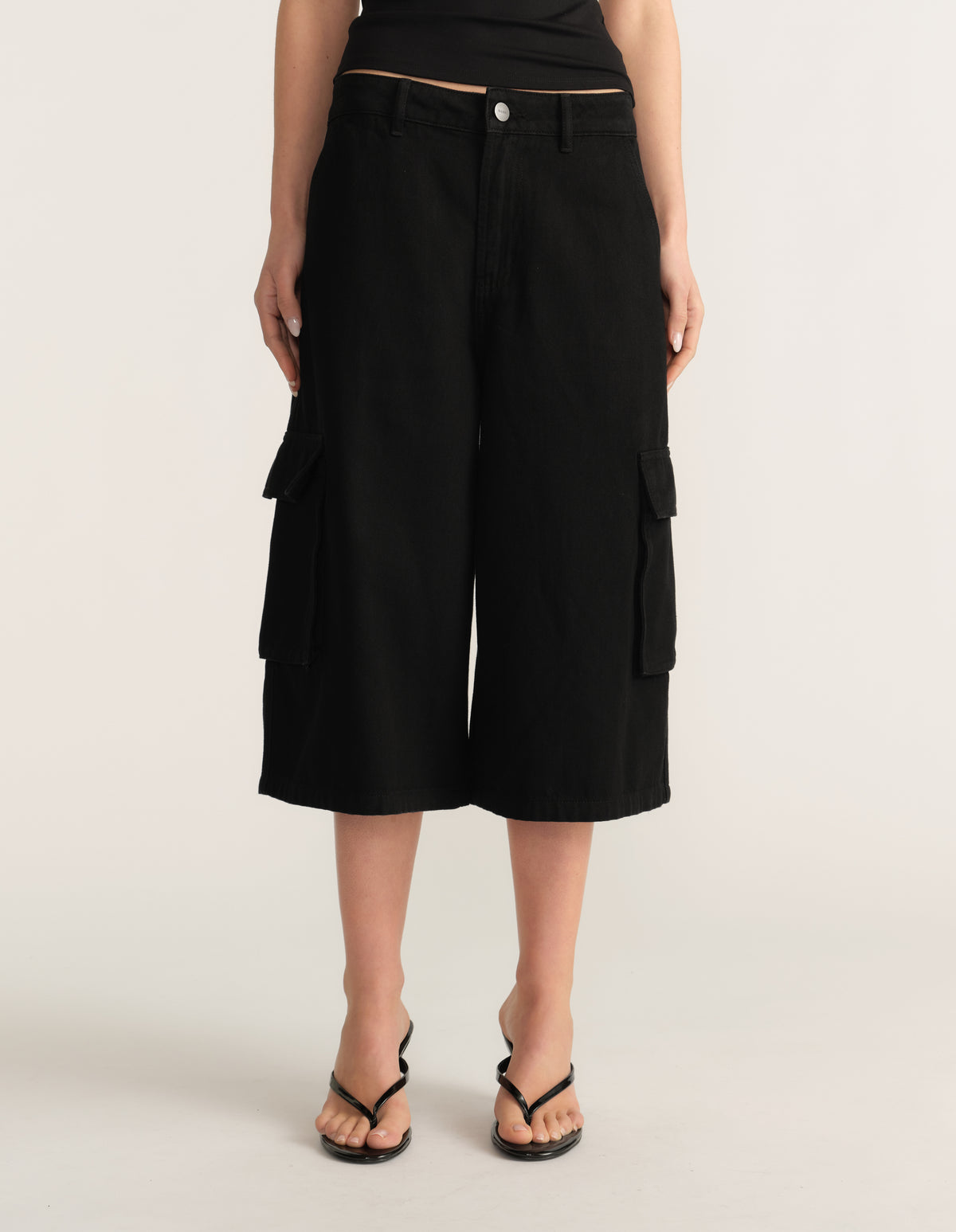Model wearing black denim cargo shorts with wide legs, utility pockets and black sandals