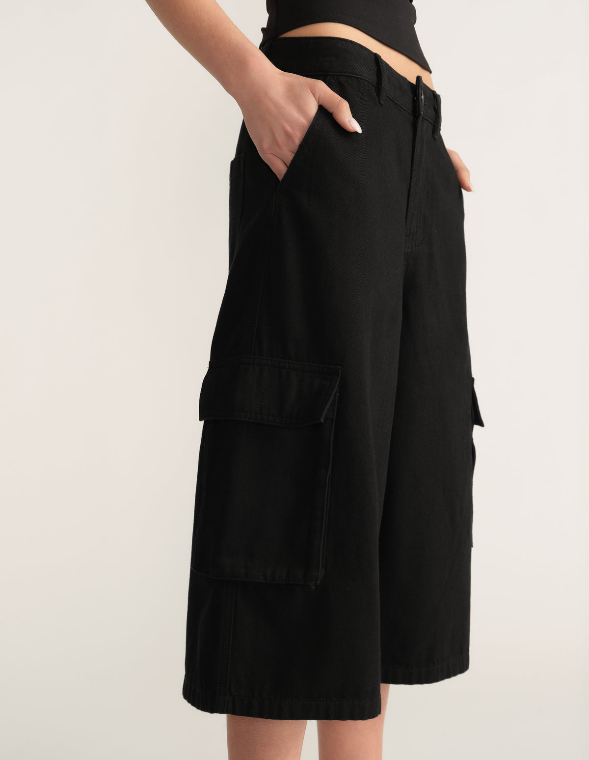 Model wearing black denim cargo shorts with a mid waist and multiple utility pockets