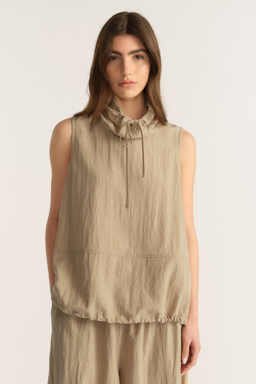 Woman wearing a beige sleeveless funnel neck top with tie details and matching relaxed pants