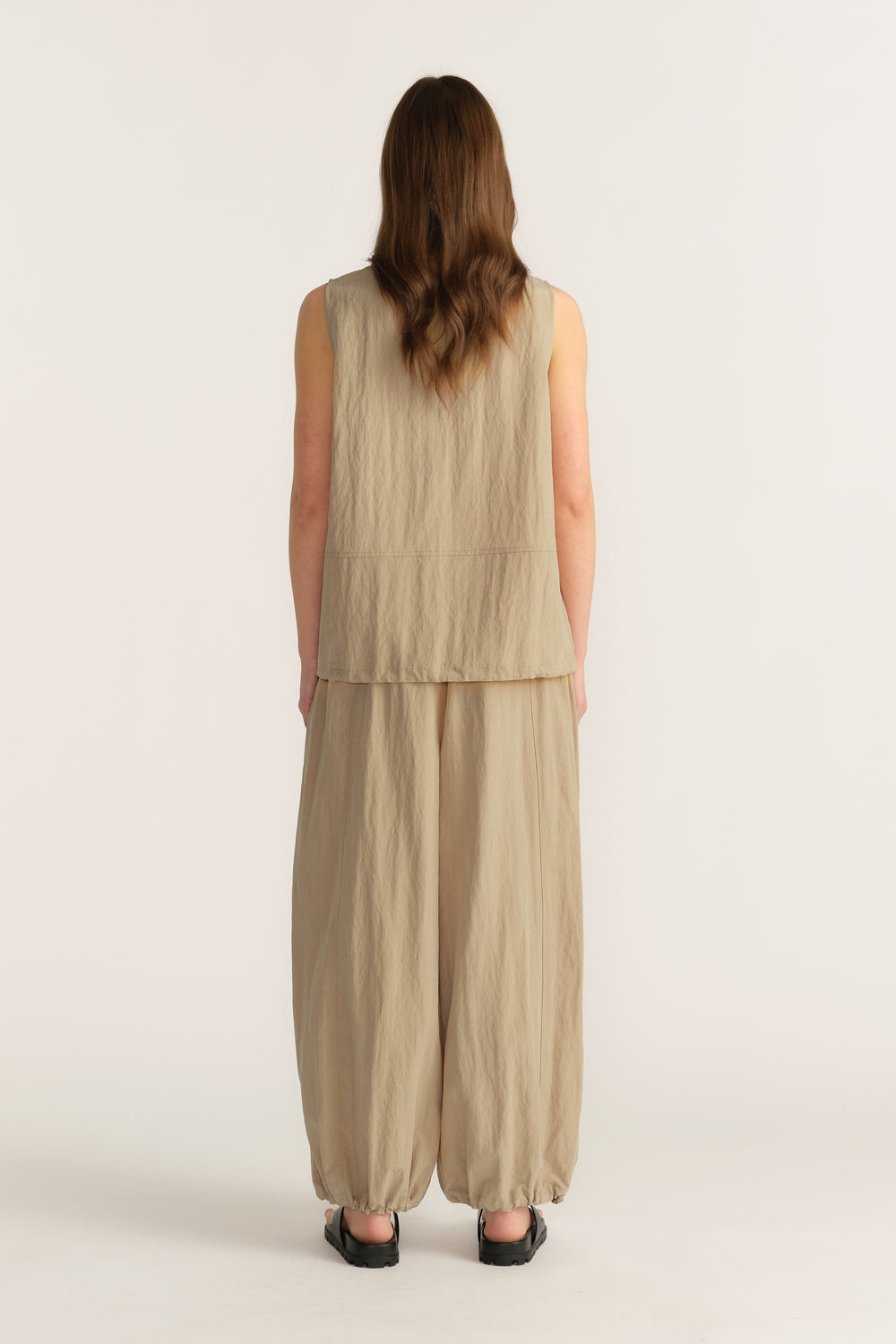 Back view of a woman wearing a beige sleeveless top with wide-leg pants and a relaxed fit