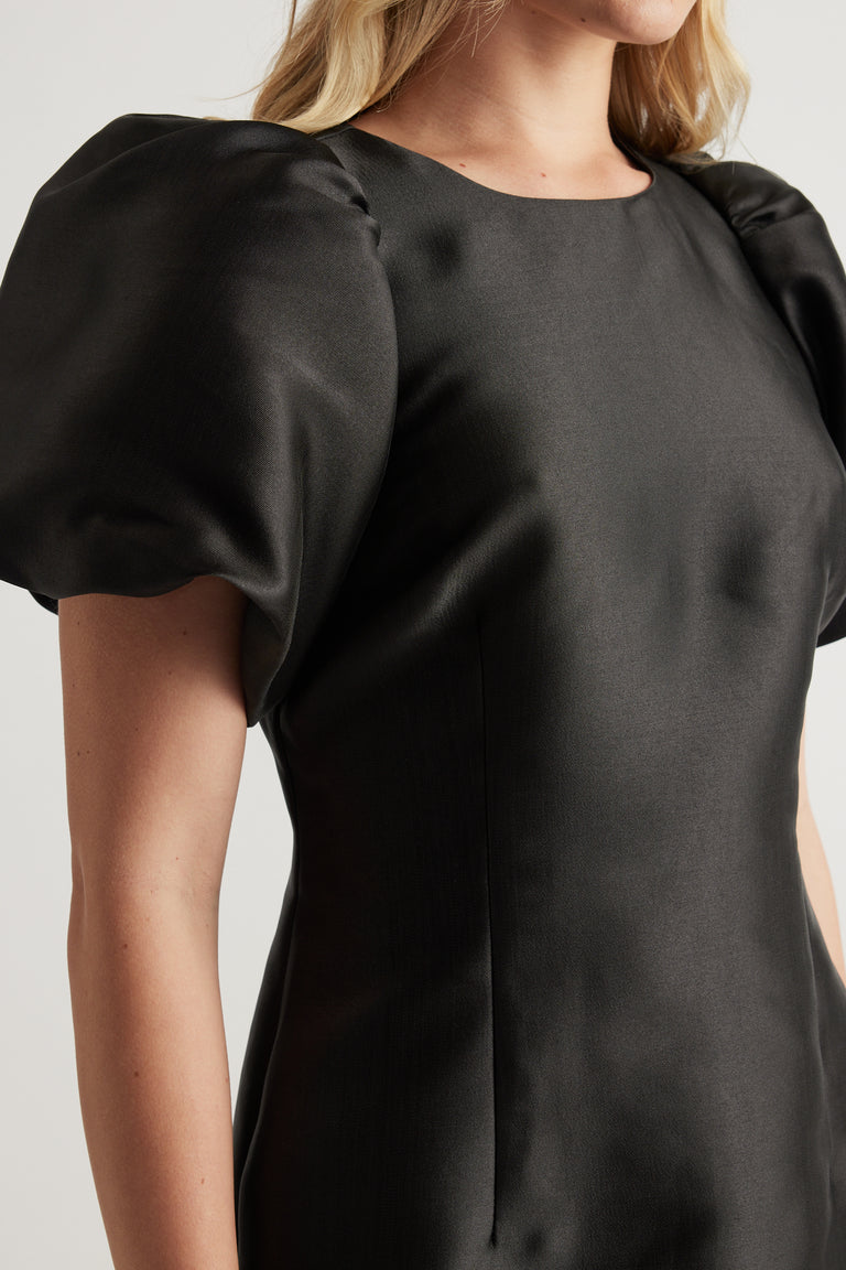 Woman wearing a black mini dress with short puff sleeves and a crew neckline