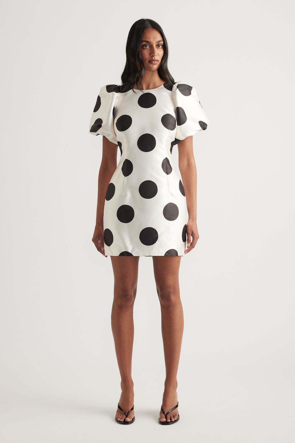 Woman wearing a white mini dress with black polka dots and puff sleeves