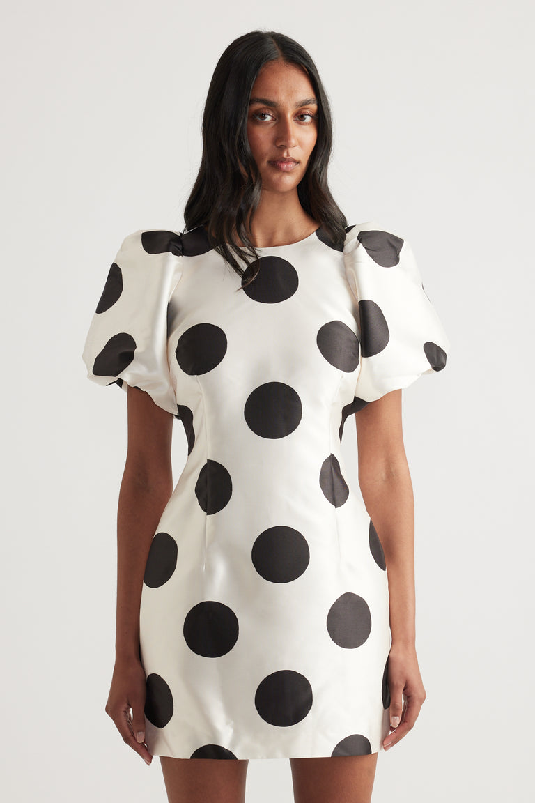Woman wearing a cream mini dress with black polka dots and short puff sleeves