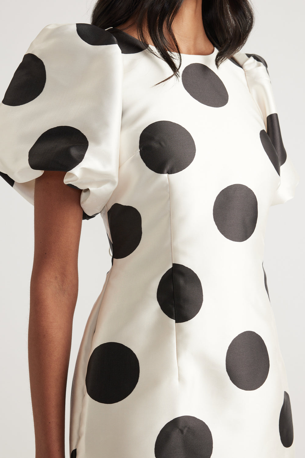 Woman wearing a cream mini dress with black polka dots and short puff sleeves
