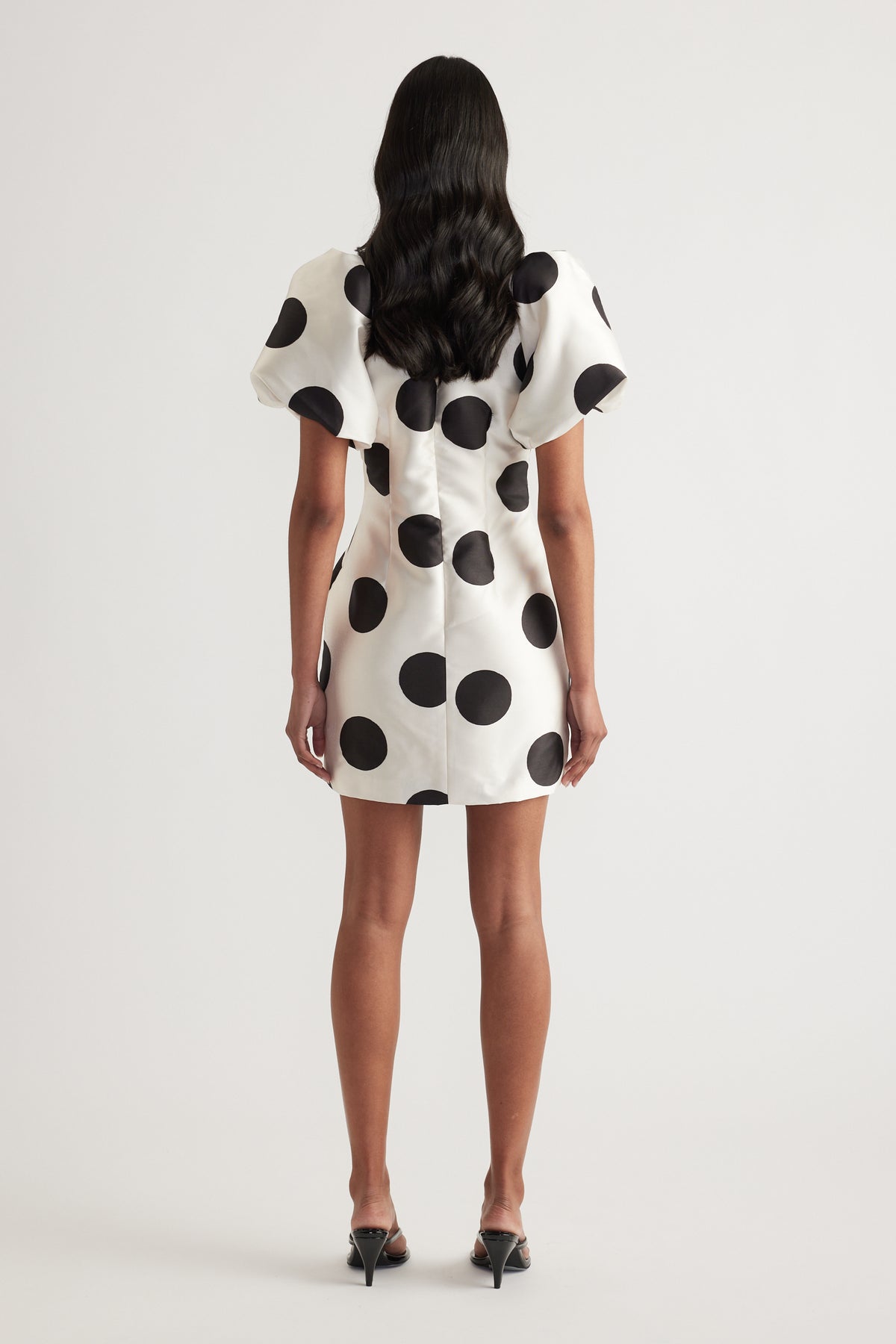 Woman wearing a cream mini dress with black polka dots and puff sleeves, viewed from behind