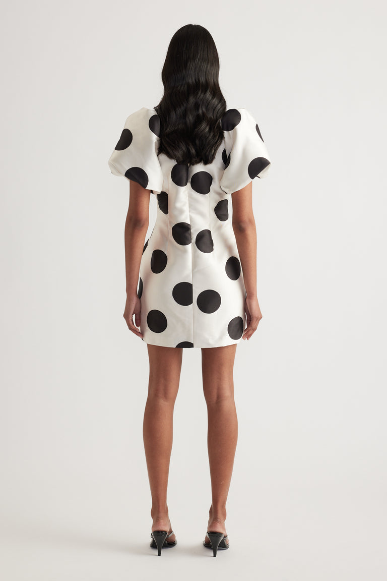 Woman wearing a cream mini dress with black polka dots and puff sleeves, viewed from behind