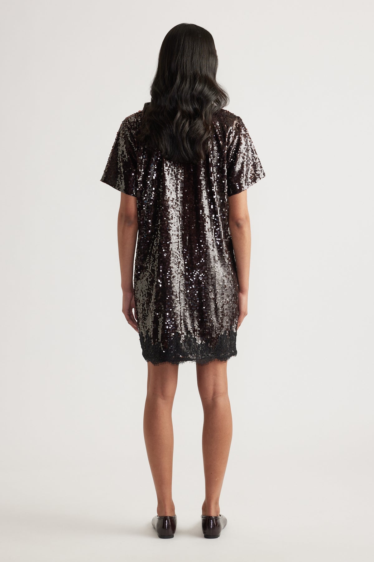 Woman wearing a black sequin short sleeve mini dress with a relaxed fit and scalloped hem