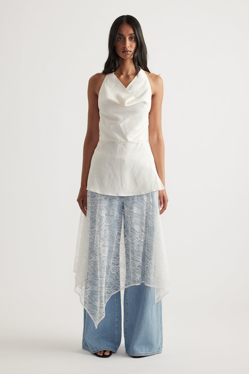 Woman wearing a white lace midi skirt over wide leg jeans with a draped asymmetric hem